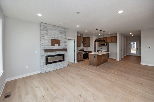 kitchen with a center island with sink, appliances with stainless steel finishes, pendant lighting, sink, and wall chimney range hood