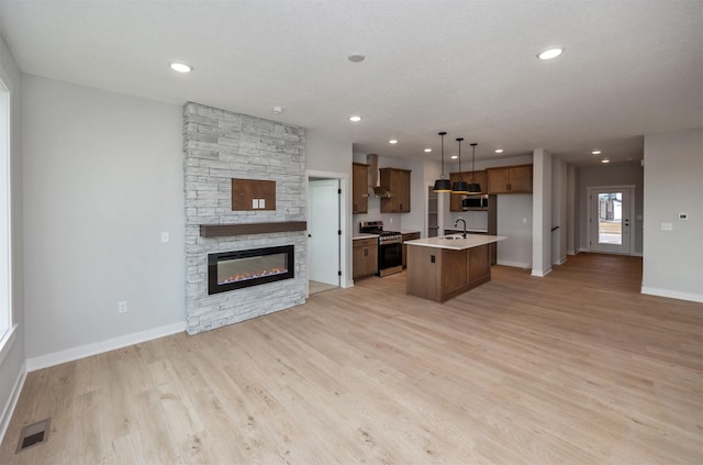 kitchen with wall chimney exhaust hood, sink, decorative light fixtures, a center island with sink, and stainless steel appliances