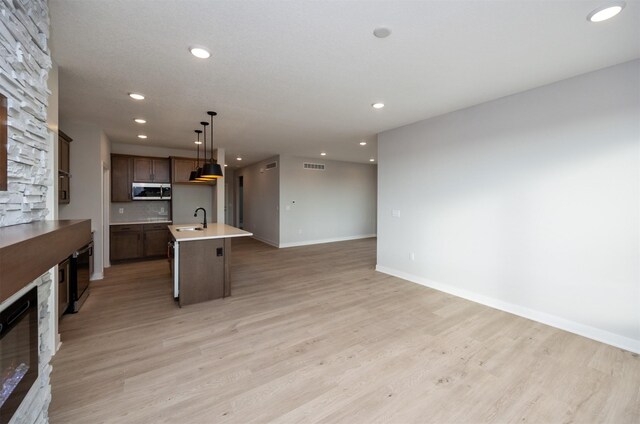 kitchen featuring light hardwood / wood-style flooring, decorative light fixtures, a center island with sink, a fireplace, and sink