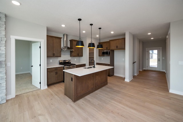 kitchen with wall chimney exhaust hood, sink, decorative light fixtures, stainless steel appliances, and a kitchen island with sink