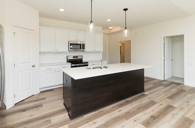 kitchen with white cabinets, sink, stainless steel appliances, and an island with sink