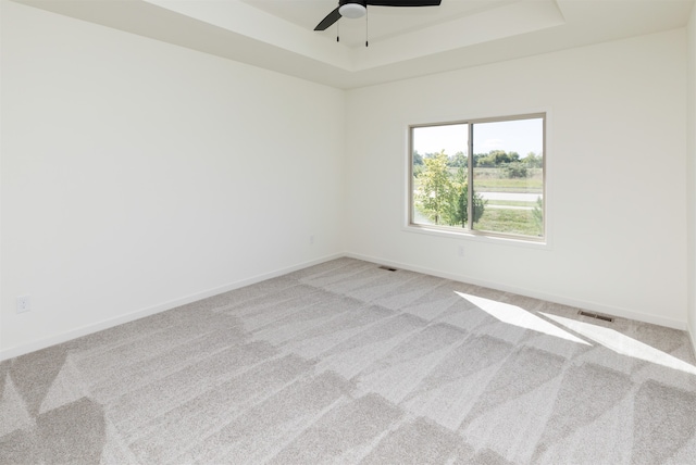 empty room with light colored carpet, a raised ceiling, and ceiling fan