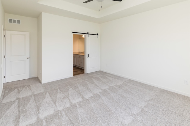 unfurnished bedroom featuring light carpet, a barn door, ensuite bath, and ceiling fan