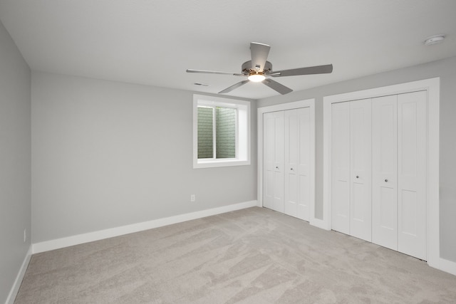 unfurnished bedroom featuring ceiling fan, light colored carpet, and two closets