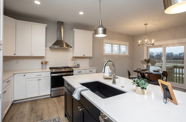 kitchen featuring white cabinets, sink, wall chimney exhaust hood, decorative light fixtures, and stainless steel range oven