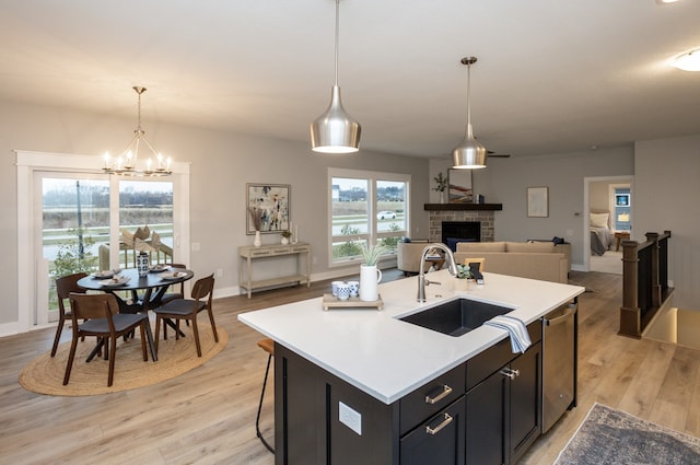 kitchen with pendant lighting, sink, a brick fireplace, light hardwood / wood-style flooring, and an island with sink