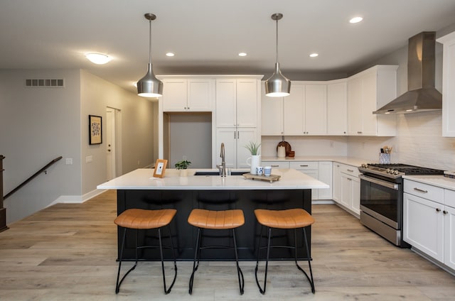 kitchen with stainless steel gas range oven, wall chimney range hood, and an island with sink