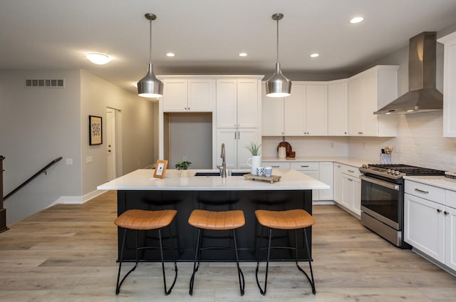 8908 Beery Pl, Johnston, IA 50131 - kitchen featuring stainless steel gas range oven, wall chimney range hood, a kitchen breakfast bar, white cabinetry, and recessed lighting