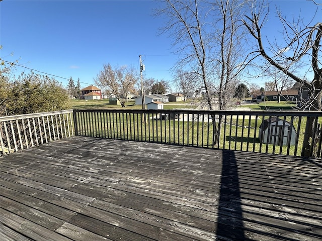 wooden terrace featuring an outbuilding, a lawn, a residential view, and a shed