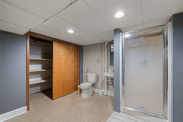 bathroom featuring sink, a drop ceiling, a shower with shower door, and toilet