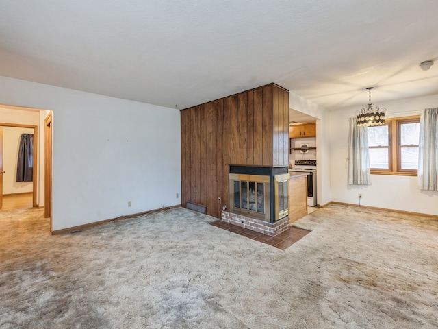 unfurnished living room with carpet flooring, a large fireplace, wooden walls, and a notable chandelier