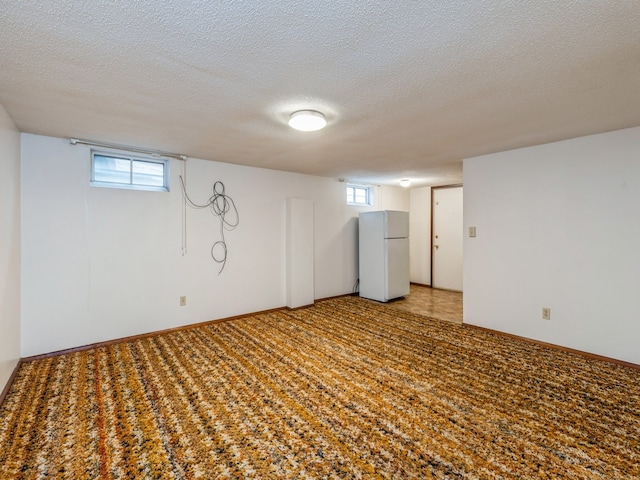 basement with plenty of natural light, white fridge, and a textured ceiling