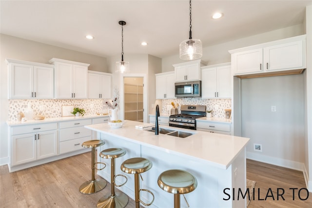 kitchen featuring white cabinets, decorative light fixtures, stainless steel appliances, and light hardwood / wood-style flooring