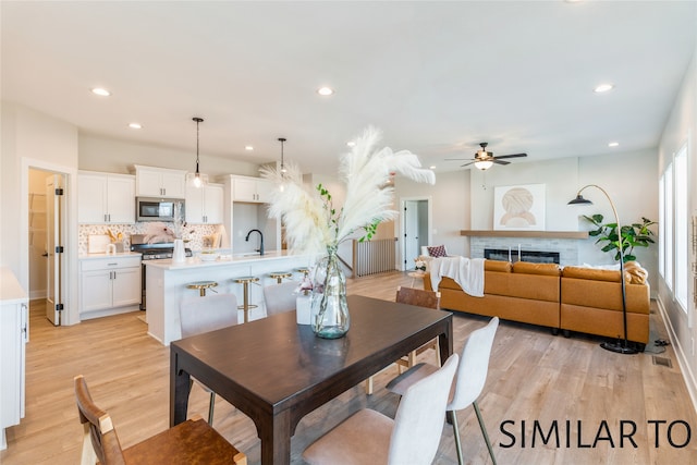 dining area with a brick fireplace, ceiling fan, light hardwood / wood-style flooring, and sink