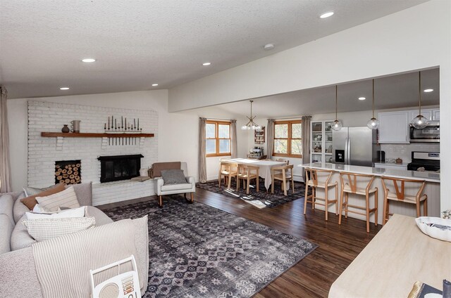 living room with dark hardwood / wood-style flooring, a textured ceiling, vaulted ceiling, a fireplace, and a chandelier