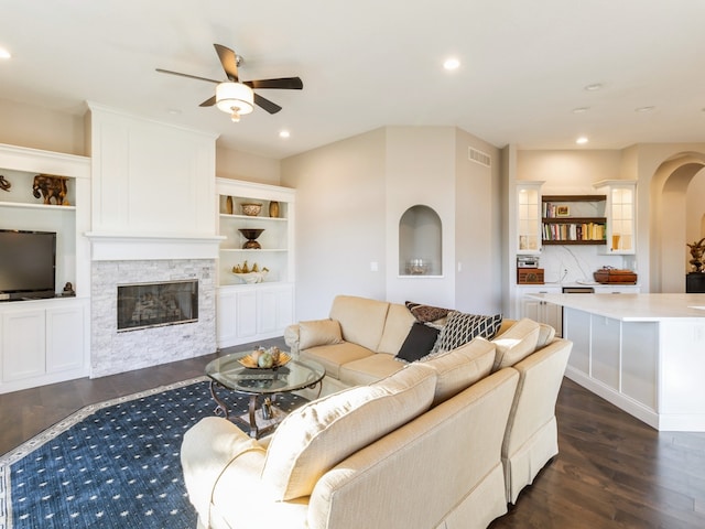 living room featuring a fireplace, built in shelves, dark hardwood / wood-style floors, and ceiling fan