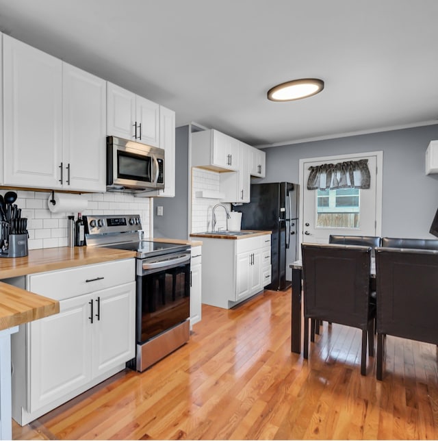 kitchen with stainless steel appliances, white cabinetry, sink, and wooden counters