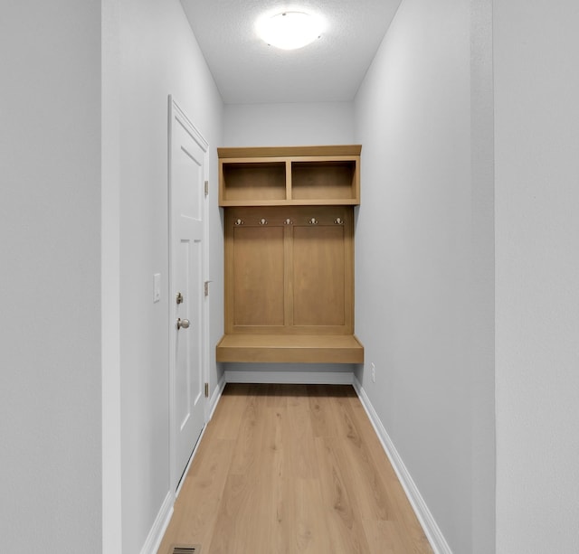 mudroom with light wood-style floors, baseboards, and a textured ceiling