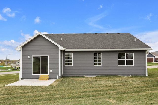 rear view of house with entry steps, a patio area, a shingled roof, and a yard