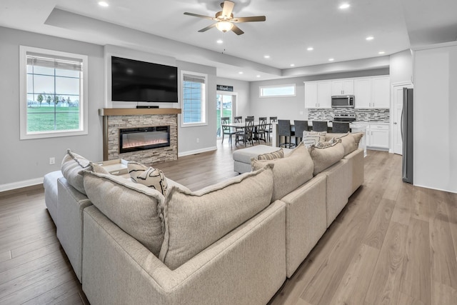 living area featuring light wood finished floors, recessed lighting, ceiling fan, a stone fireplace, and baseboards