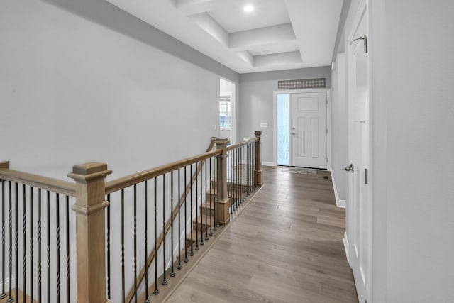 hallway featuring a tray ceiling, wood finished floors, an upstairs landing, and baseboards