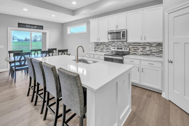 kitchen with a center island with sink, light wood-style flooring, appliances with stainless steel finishes, a breakfast bar, and a sink