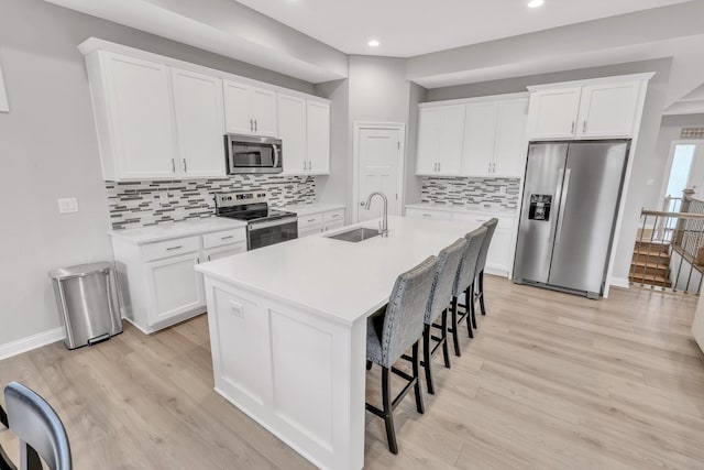 kitchen with a breakfast bar area, stainless steel appliances, a sink, light wood-type flooring, and an island with sink