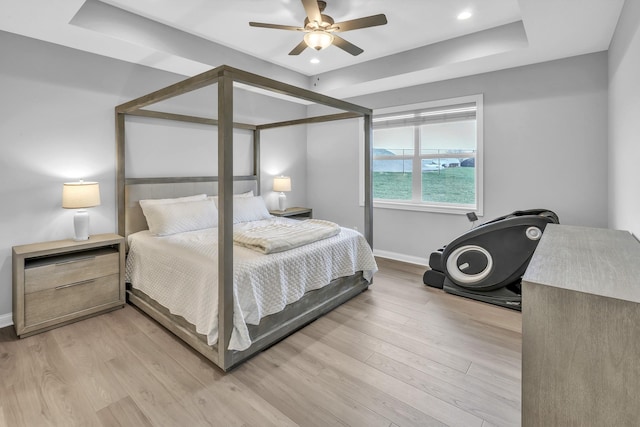 bedroom with a tray ceiling, baseboards, and light wood finished floors