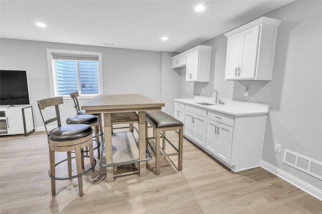 kitchen featuring light wood finished floors, visible vents, white cabinets, light countertops, and a sink