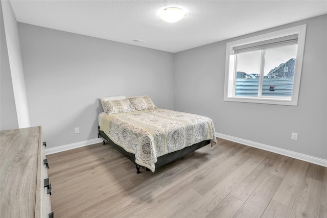 bedroom with a textured ceiling, wood finished floors, and baseboards