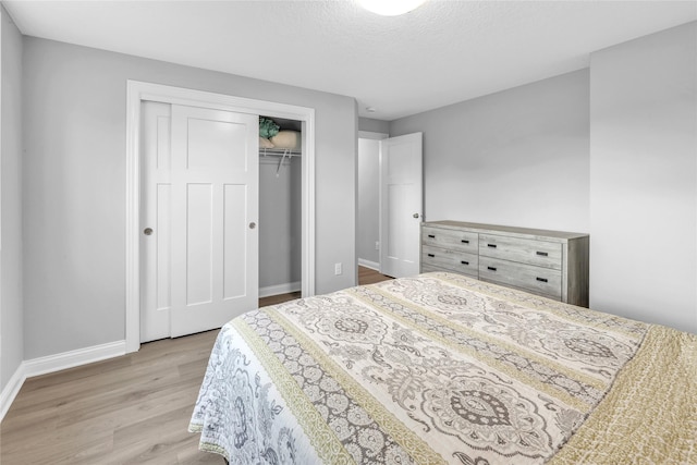 bedroom with light wood-style floors, a textured ceiling, baseboards, and a closet