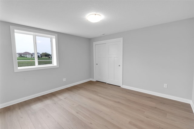 unfurnished bedroom with a textured ceiling, light wood finished floors, a closet, and baseboards