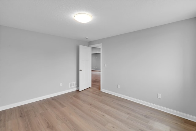 unfurnished room featuring light wood-style floors, visible vents, a textured ceiling, and baseboards