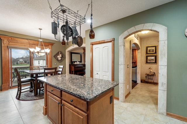 kitchen with a kitchen island, dark stone counters, a textured ceiling, and an inviting chandelier