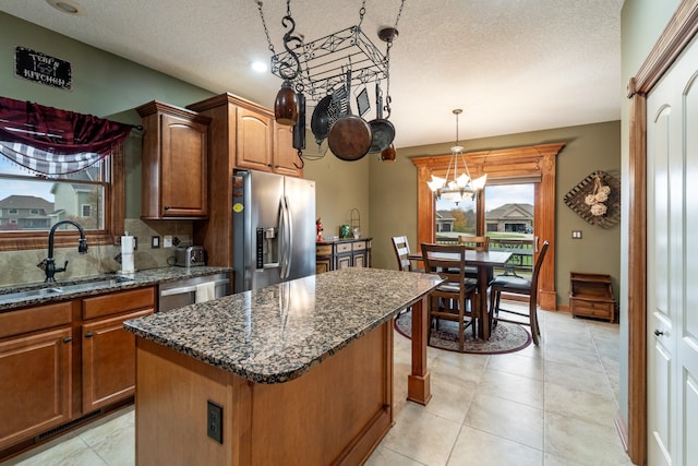 kitchen with appliances with stainless steel finishes, a textured ceiling, sink, decorative light fixtures, and a center island