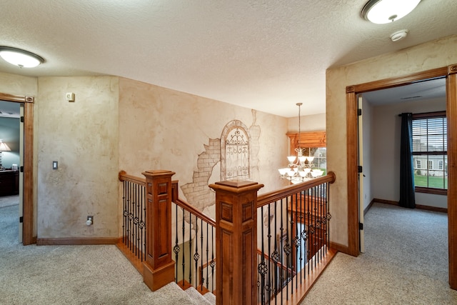 hallway featuring a textured ceiling, light colored carpet, and an inviting chandelier