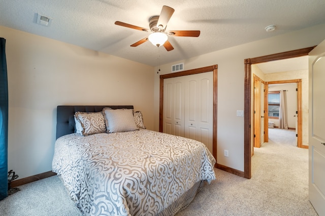 bedroom with ceiling fan, a textured ceiling, light carpet, and a closet