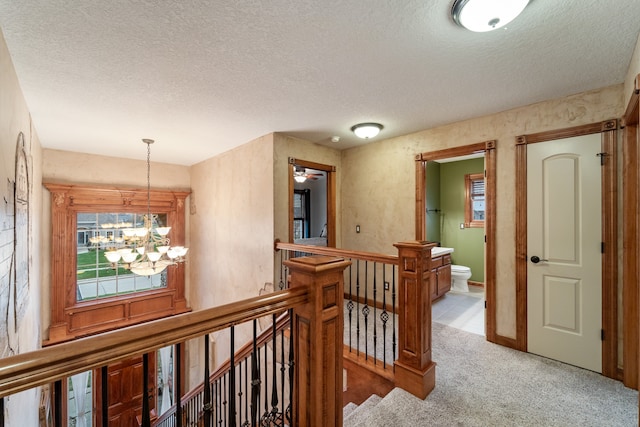 hallway with a notable chandelier, light colored carpet, and a textured ceiling