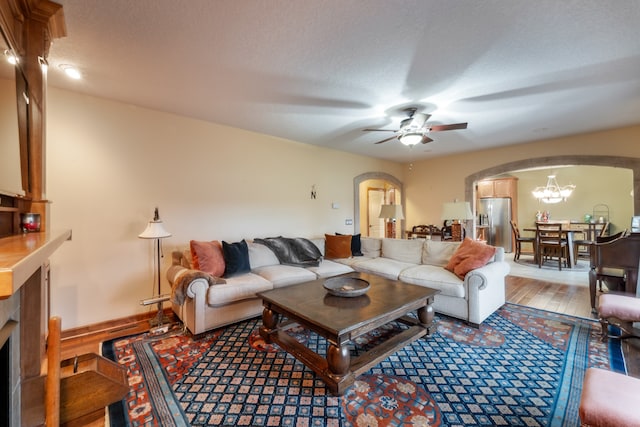 living room featuring ceiling fan with notable chandelier, a textured ceiling, and light wood-type flooring