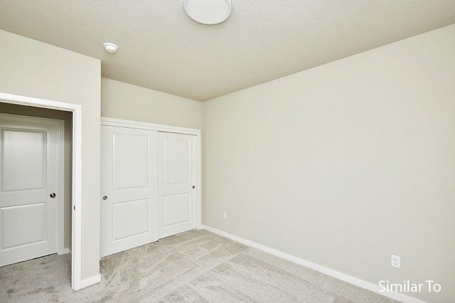 unfurnished bedroom with light colored carpet, a closet, and a textured ceiling