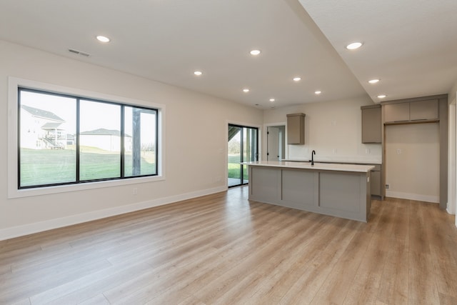 kitchen with gray cabinetry, an island with sink, and light hardwood / wood-style floors