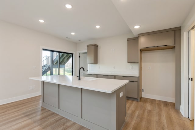 kitchen with gray cabinets, a kitchen island with sink, sink, and light hardwood / wood-style floors