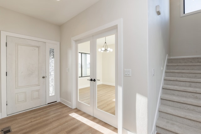 foyer with french doors, light hardwood / wood-style floors, and an inviting chandelier