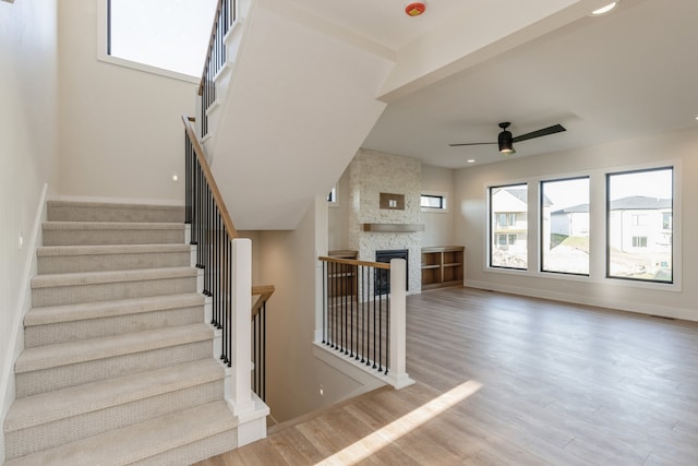 staircase with ceiling fan, a stone fireplace, and wood-type flooring