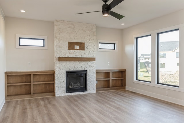 unfurnished living room featuring a stone fireplace, ceiling fan, and light wood-type flooring