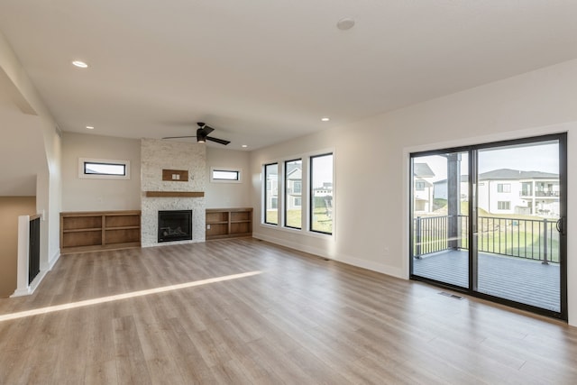 unfurnished living room with light hardwood / wood-style floors, a stone fireplace, and ceiling fan