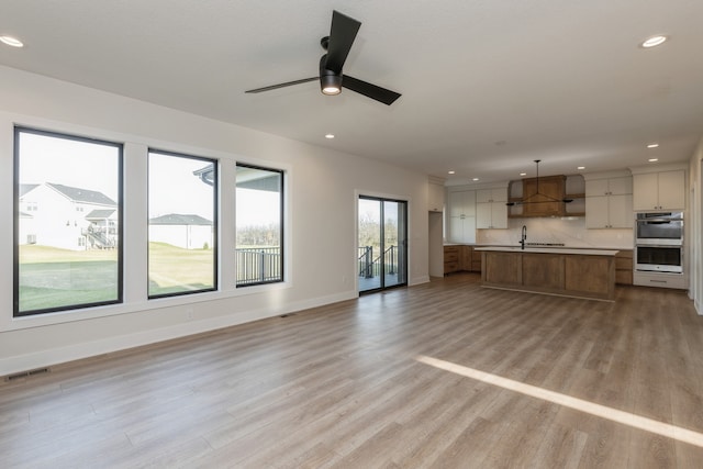 unfurnished living room featuring ceiling fan, sink, and light wood-type flooring