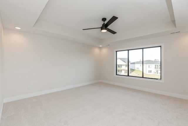 unfurnished room featuring a tray ceiling, ceiling fan, and light carpet