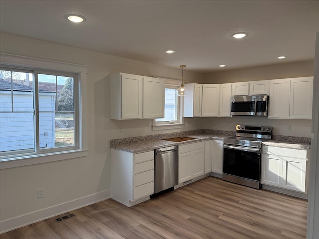 kitchen featuring white cabinetry, sink, stainless steel appliances, decorative light fixtures, and light wood-type flooring