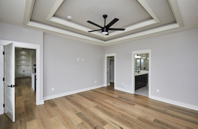 unfurnished bedroom with light wood-style flooring, visible vents, a spacious closet, ensuite bath, and a raised ceiling